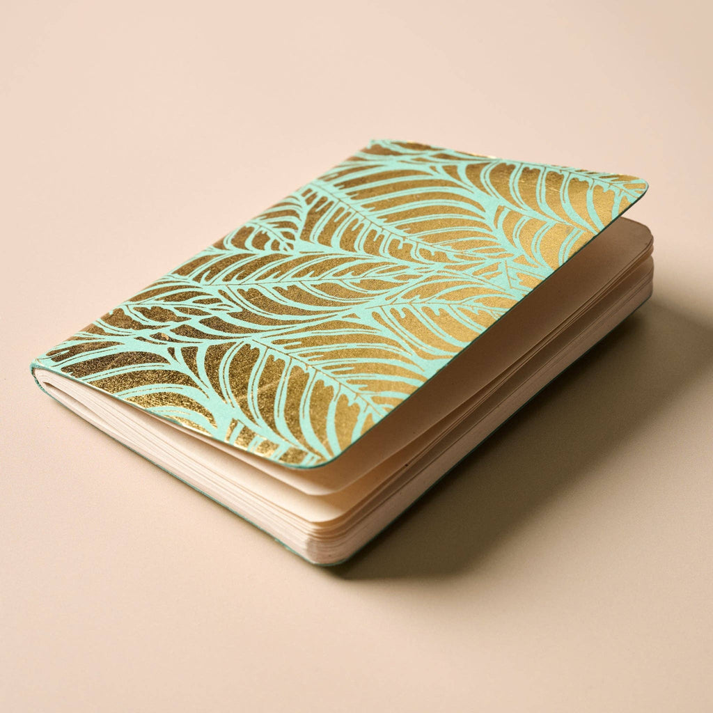 Notebook with gold leaf pattern on turquoise background.