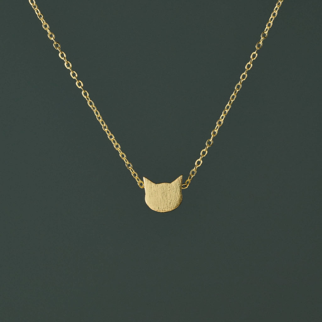 Gold plated brass minimal cat face shaped pendant necklace on a dark green background